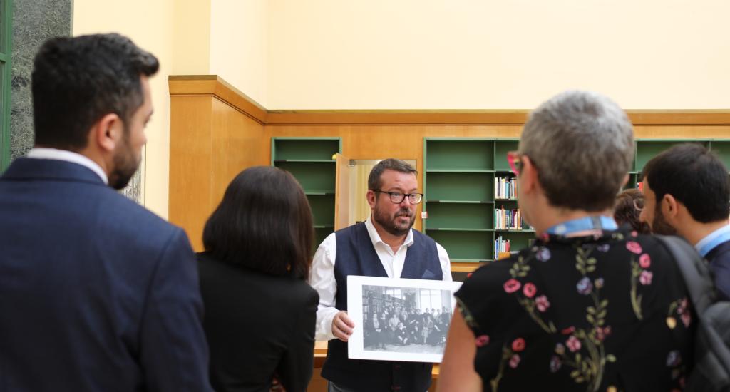 This photo shows guests at a Commons event on a tour of the Library. A staff member shares photos about the history of the Library. 