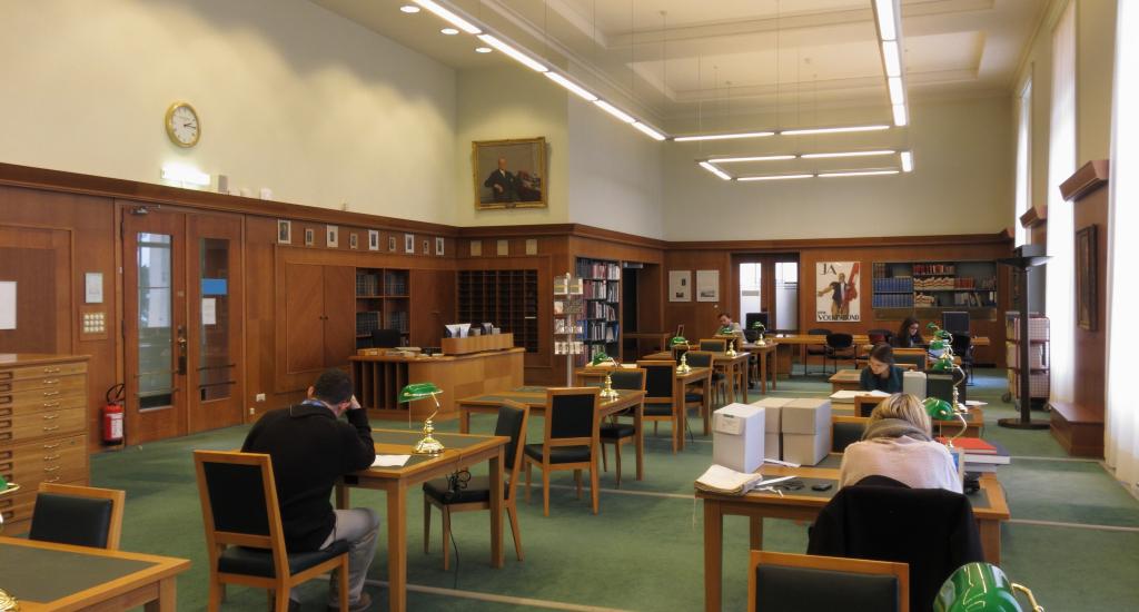 This is an image of the Reading Room at the UN Archives Geneva, where researchers can come to consult physical documents. The photo shows the room and desks where researchers can sit and consult documents. In the room are several students and Archives staff members.