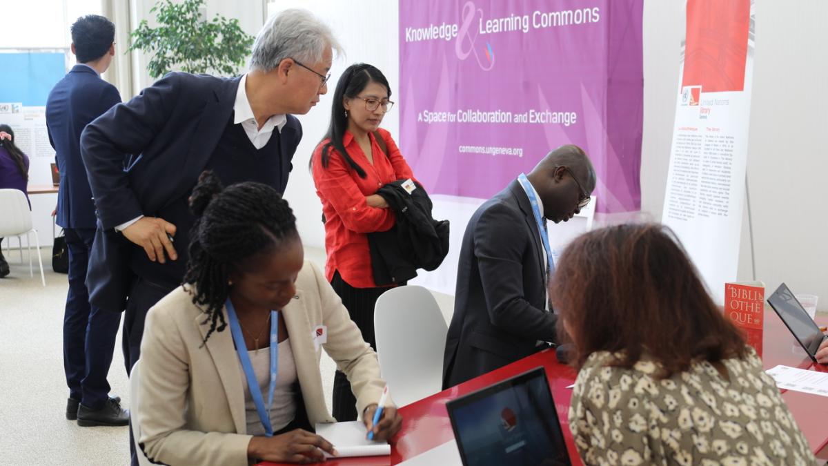 This is a photo from the event. Four diplomats are shown, looking at Library resources on a table, while a Librarian shares information while sitting behind her laptop. 
