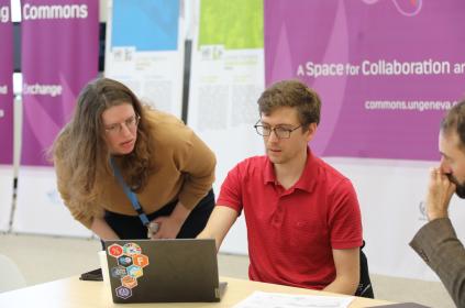 This is a photo from the day of the hackathon. A librarian assists one of the participants with a question as they look at resources on a laptop.