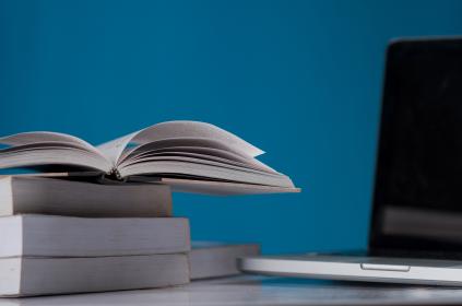 Picture of a couple books stacked with an open book on top and a laptop in the background