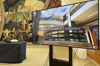 This photo shows a TV screen with the name if the conference: META-UN Launch Conference. The backdrop is the Library Events Room at the UN Library & Archives Geneva.