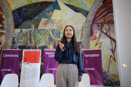 This is a photo of a woman moderating an event at the Library. She is holding a microphone and looking out at the audience.