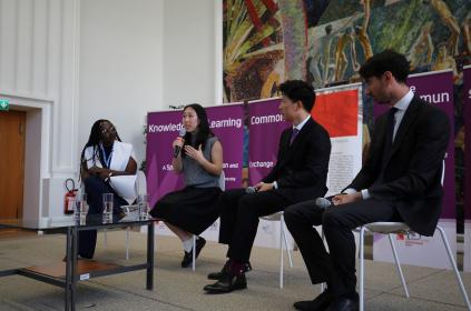 A panel of four young professionals is seated in the Library for a discussion on young people and multilateralism. One young woman is holding a microphone and speaking to the audience.